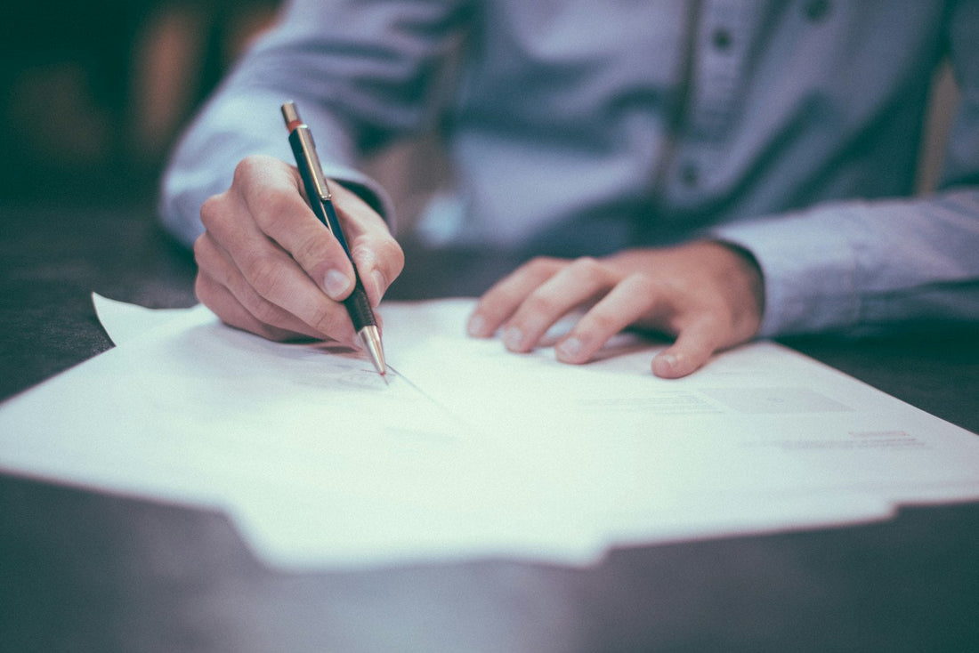 A person sitting at a desk writing a letter by hand with a pen on white paper