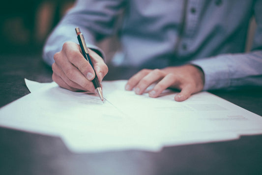 A person sitting at a desk writing a letter by hand with a pen on white paper