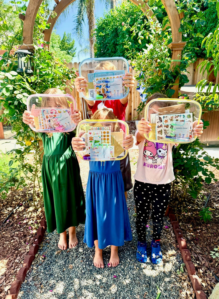 4 children all standing in a garden holding a Little Letter Box out in front of their faces